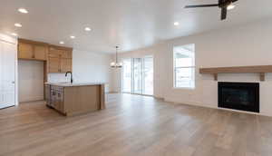 Kitchen with light hardwood / wood-style flooring, sink, a fireplace, ceiling fan with notable chandelier, and an island with sink