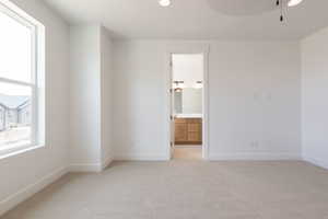 Unfurnished bedroom featuring light carpet, ensuite bath, and ceiling fan