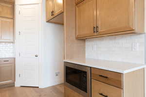 Kitchen featuring light wood-type flooring, black microwave, and tasteful backsplash