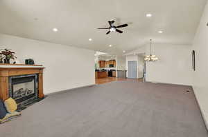 Great room with high ceiling, ceiling fan with notable chandelier over formal dining area, carpet, and a fireplace