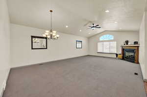 Great room with a textured ceiling, ceiling fan, dining area with chandelier, lofted ceiling, and carpet flooring