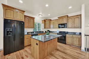 Kitchen with granite countertops, black appliances, sink, recently refinished hardwood floors, and a center island.