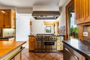 Kitchen with decorative backsplash, dark tile patterned floors, double oven range, and ventilation hood