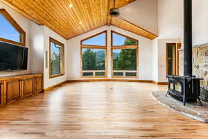 Unfurnished living room featuring a wood stove, high vaulted ceiling, wooden ceiling, and light wood-type flooring, mountain and ski area views.