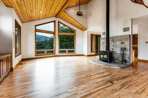 Unfurnished living room with a wood stove, light wood-type flooring, high vaulted ceiling, a mountain view, and wood ceiling