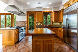 Kitchen with light tile patterned floors, a kitchen island, decorative backsplash, high quality appliances, and island range hood