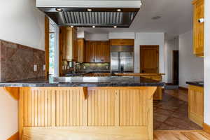 Kitchen with kitchen peninsula, light hardwood / wood-style flooring, stainless steel built in fridge, and tasteful backsplash