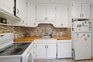 Kitchen with decorative backsplash, white appliances, sink, and white cabinets