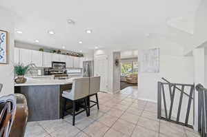 Kitchen featuring appliances with stainless steel finishes, a breakfast bar, kitchen peninsula, light tile patterned floors, and white cabinetry