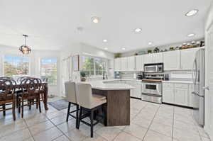 Kitchen featuring appliances with stainless steel finishes, decorative light fixtures, light tile patterned floors, a kitchen breakfast bar, and white cabinetry