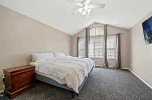 Carpeted bedroom featuring ceiling fan and vaulted ceiling