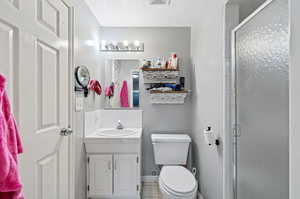 Bathroom featuring tile patterned flooring, a shower with shower door, toilet, and vanity