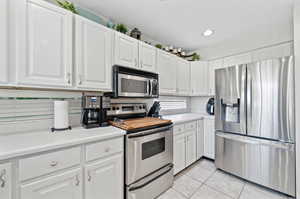 Kitchen featuring appliances with stainless steel finishes, light tile patterned floors, and white cabinets