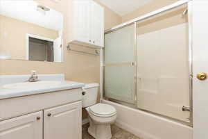 Full bathroom featuring toilet, tile patterned floors, shower / bath combination with glass door, and vanity