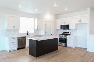 Kitchen with white cabinets, stainless steel appliances, a center island, light hardwood / wood-style flooring, and sink