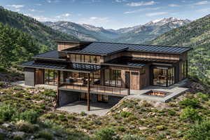 Rear view of house featuring a standing seam roof, a fire pit, a patio, stone siding, and a mountain view