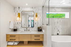 Bathroom featuring a bath, vanity, and tile walls