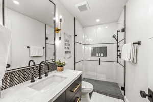 Bathroom with vanity, toilet, a shower with door, and tasteful backsplash