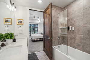 Bathroom with tile patterned flooring, double sink vanity, shower / bath combination with glass door, and ceiling fan