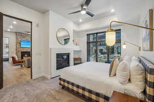 Bedroom with a stone fireplace, light hardwood / wood-style floors, and ceiling fan