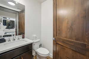 Bathroom featuring hardwood / wood-style flooring, toilet, vanity, and stacked washing maching and dryer