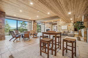 Tiled dining space featuring an outdoor stone fireplace and wooden ceiling