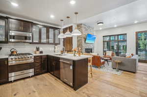 Kitchen featuring stainless steel appliances, a fireplace, kitchen peninsula, decorative backsplash, and light wood-type flooring