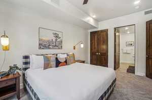 Bedroom with ceiling fan, connected bathroom, and light colored carpet