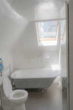 Bathroom featuring toilet, tile patterned floors, and lofted ceiling with skylight