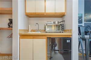 Bar featuring black refrigerator, sink, and white cabinets