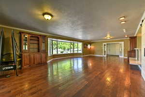 Unfurnished living room with a textured ceiling, dark hardwood / wood-style flooring, and ornamental molding