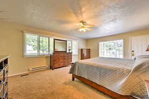 Bedroom with baseboard heating, light colored carpet, and ceiling fan