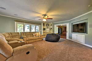 Carpeted living room featuring ornamental molding, a textured ceiling, and ceiling fan