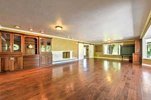 Unfurnished living room featuring ornamental molding, a barn door, a textured ceiling, and dark wood-type flooring