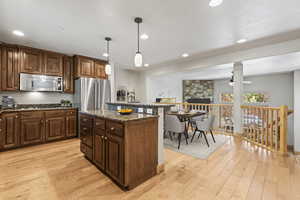 Kitchen with stainless steel appliances, light wood-type flooring, dark stone counters, a center island, and hanging light fixtures