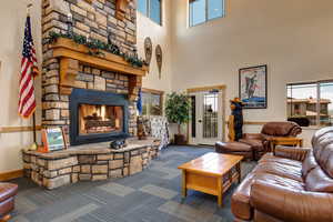 Living room with a stone fireplace, dark colored carpet, and a high ceiling