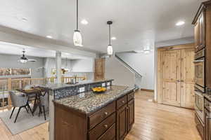 Kitchen with decorative light fixtures, light wood-type flooring, dark brown cabinets, a kitchen island, and ceiling fan