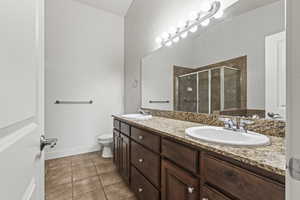 Bathroom featuring tile patterned flooring, toilet, an enclosed shower, and dual bowl vanity