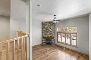 Unfurnished living room featuring a stone fireplace, hardwood / wood-style flooring, and ceiling fan