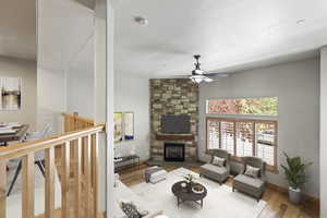 Living room featuring ceiling fan, a stone fireplace, and wood-type flooring