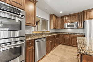 Kitchen featuring dark stone countertops, sink, light hardwood / wood-style flooring, and stainless steel appliances