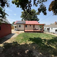 Back of house with a deck, a yard, and solar panels