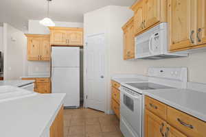 Kitchen with light brown cabinetry, white appliances, decorative light fixtures, and light tile patterned floors