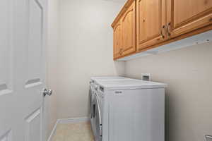 Laundry area featuring cabinets, light tile patterned floors, and washing machine and clothes dryer