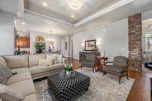 Living room featuring wood-type flooring, brick wall, decorative columns, and an inviting chandelier