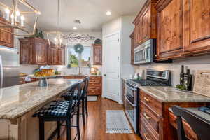 Kitchen featuring decorative light fixtures, wood-type flooring, decorative backsplash, a center island, and appliances with stainless steel finishes