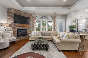 Living room with a fireplace, wood-type flooring, and a tray ceiling