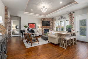 Living room featuring a fireplace, dark hardwood / wood-style floors, a tray ceiling, and a notable chandelier