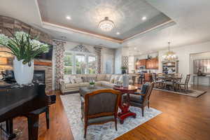 Living room with a stone fireplace, hardwood / wood-style floors, a chandelier, and a tray ceiling