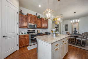 Kitchen featuring dark hardwood / wood-style flooring, white cabinets, a center island, light stone counters, and appliances with stainless steel finishes